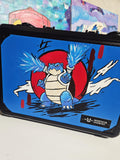 Angled front view of custom hand-painted Blastoise 3-row slab case — blue case with Blastoise firing twin water cannons against a bold red circle background, freehand acrylic artwork by 5/14 Apparel