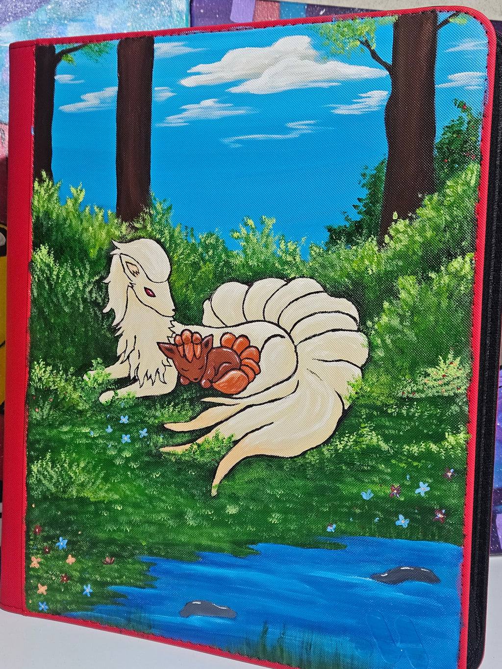 Angled view of custom hand-painted Ninetales and Vulpix Pokemon card binder — freehand acrylic artwork sealed with UV and scratch-resistant coating by 5/14 Apparel