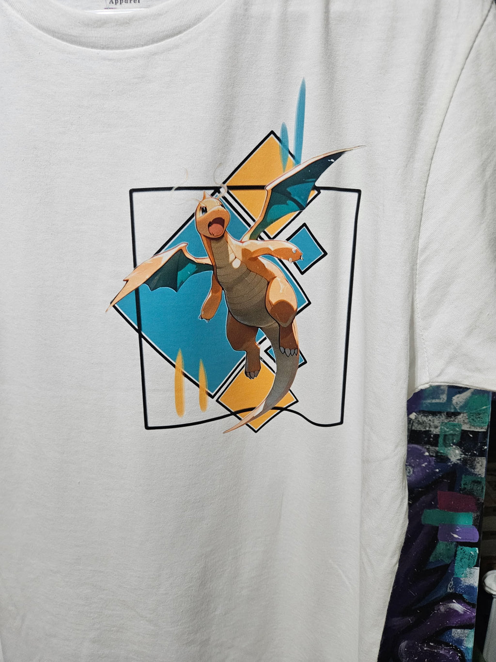 Close-up of Dragonite graphic on white tee — Dragonite bursting from geometric diamond frame with teal and gold design by 5/14 Apparel
