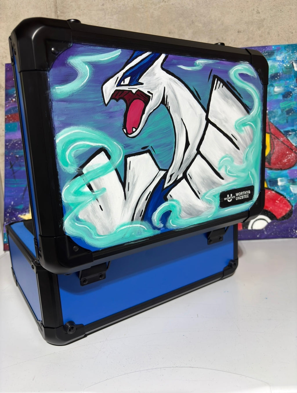 Side angle of custom hand-painted Lugia Pokemon slab case open and stacked — blue 3-row case showing Lugia acrylic artwork with teal energy trails, sealed with UV and scratch-resistant coating by 5/14 Apparel