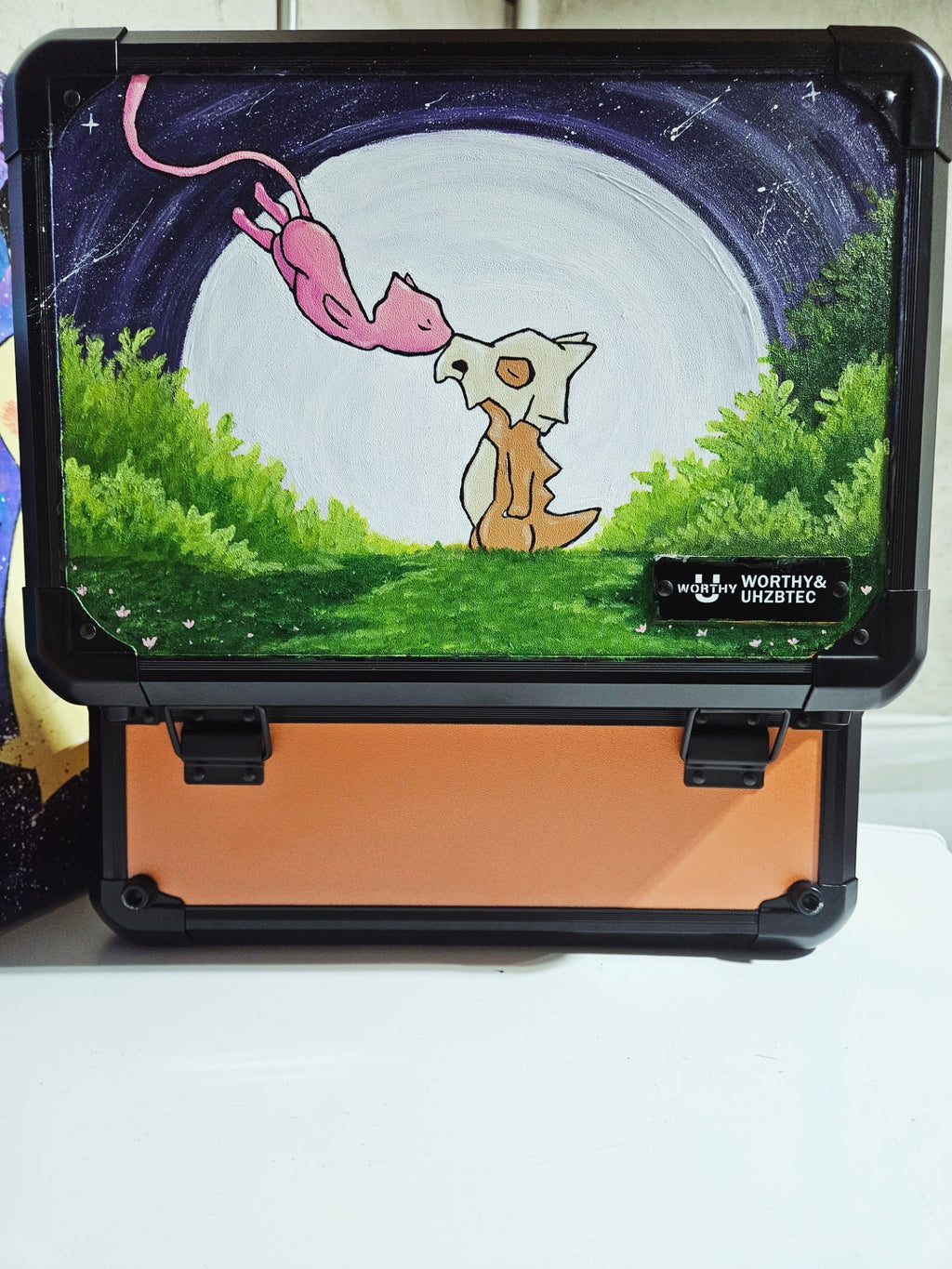 Front view of custom hand-painted Cubone and Mew 3-row orange slab case — freehand acrylic artwork featuring Mew descending toward Cubone under a full moon
