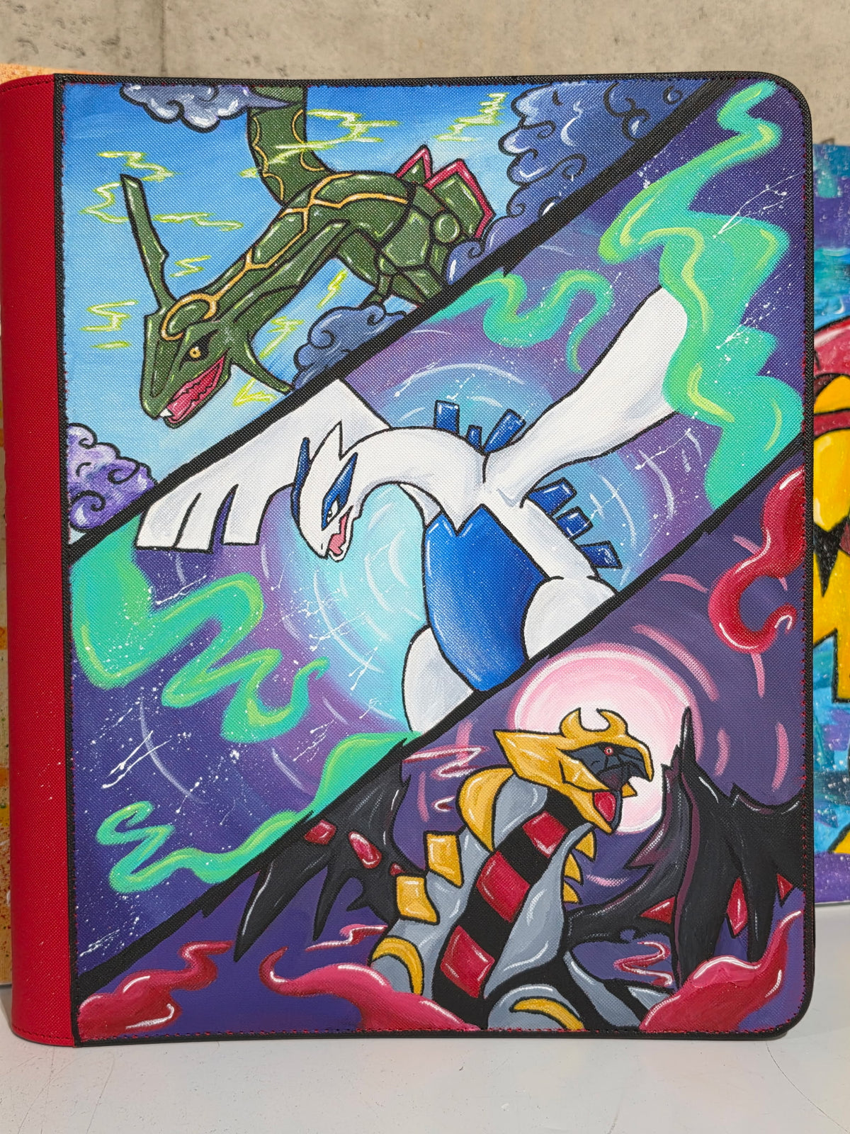 5/14 Apparel custom hand-painted Rayquaza Lugia and Giratina 9-pocket binder — three legendary split-panel diagonal composition with Rayquaza in lightning sky, Lugia in psychic energy, and Giratina in purple shadow, one-of-one acrylic art on red binder