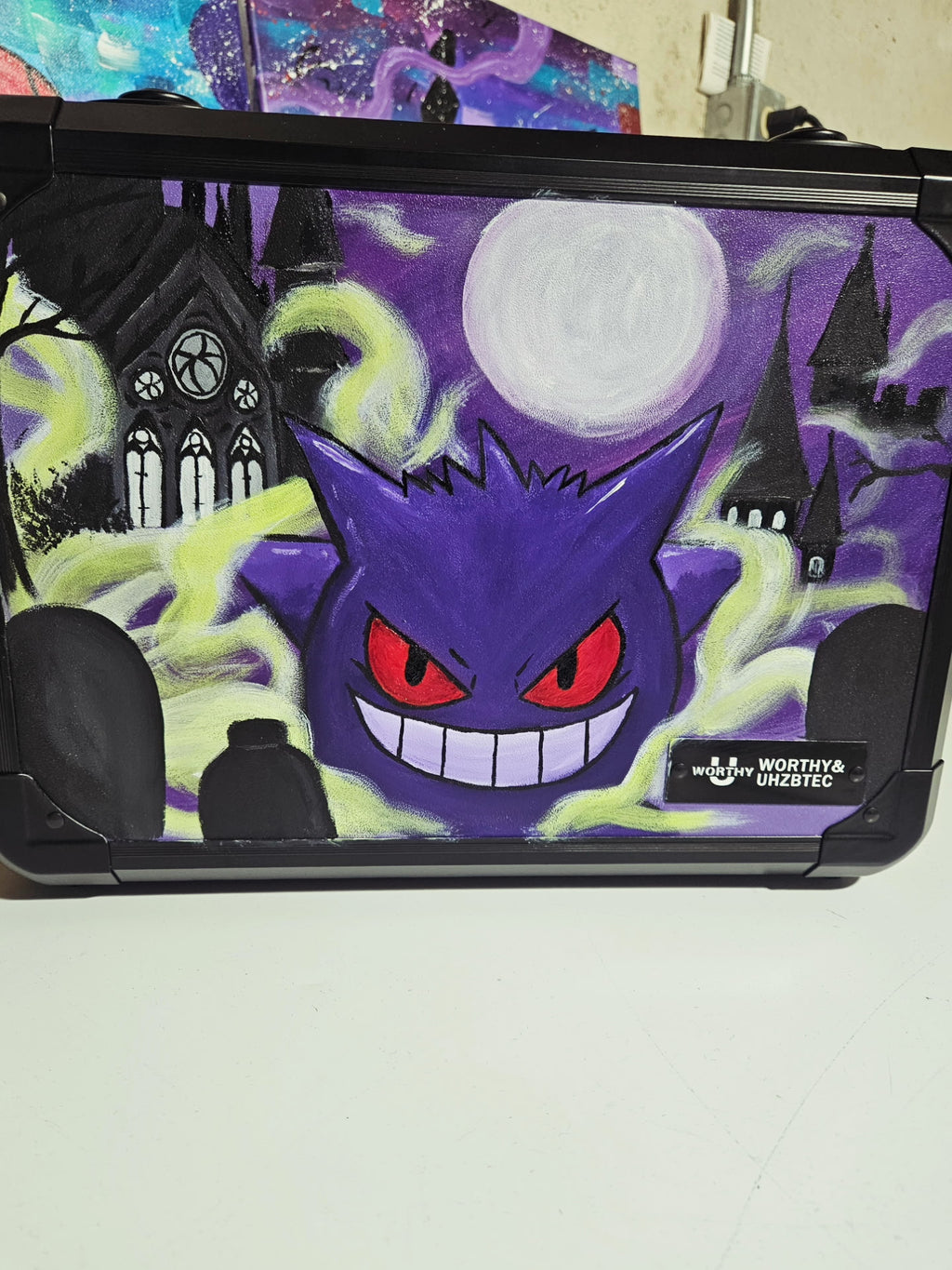 Angled view of custom hand-painted Gengar Pokemon slab case — purple 3-row case with bold Gengar acrylic artwork and glowing green energy trails, sealed with UV and scratch-resistant coating by 5/14 Apparel
