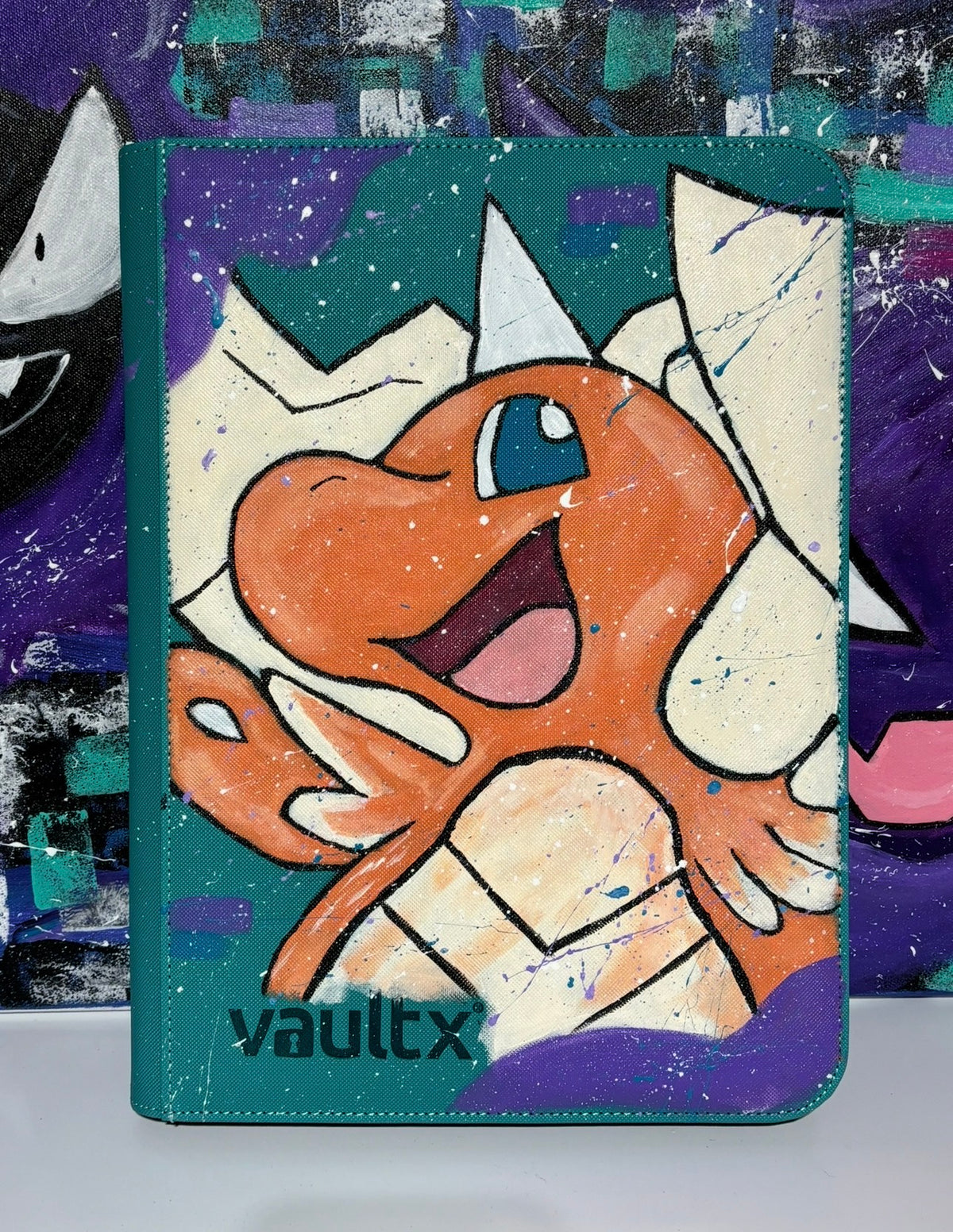 Front view of custom hand-painted Mega Dragonite VaultX binder — orange Dragonite bursting through geometric shards on teal and purple background, freehand acrylic artwork by 5/14 Apparel