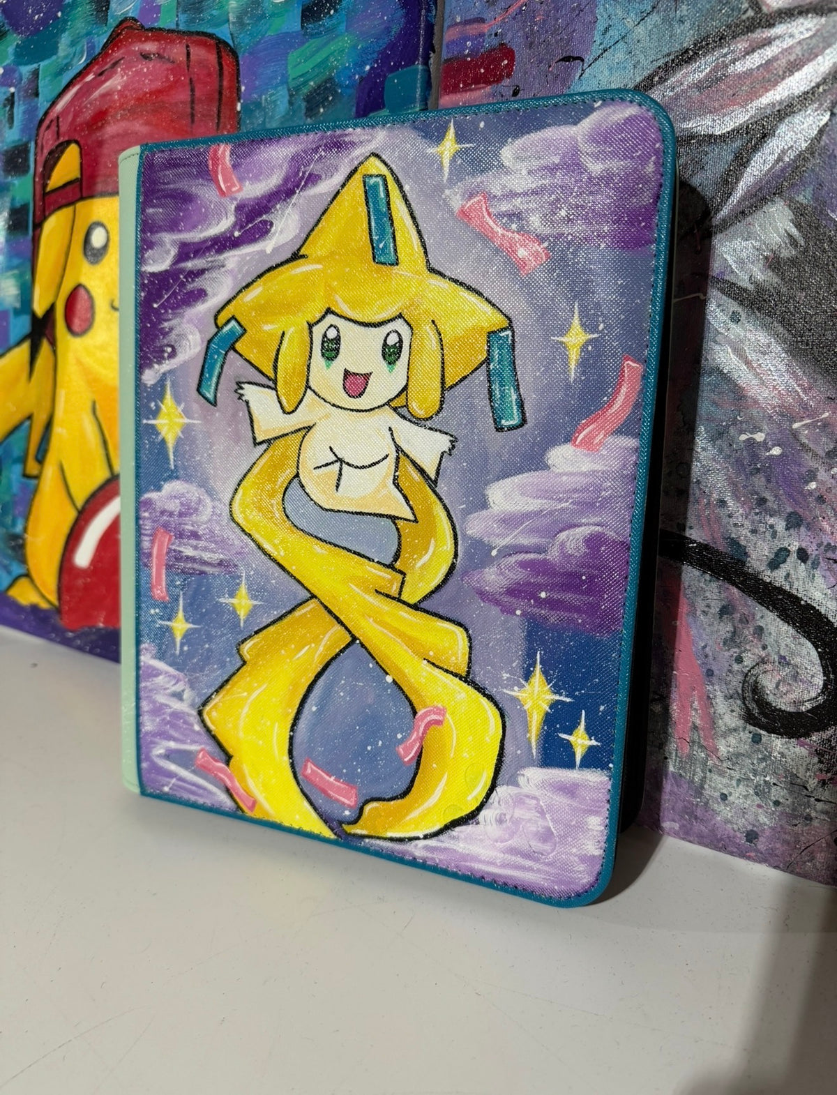 5/14 Apparel Custom Jirachi Binder — Angled view hand-painted Jirachi floating in a purple starlit sky, freehand acrylic art on light green top loader binder