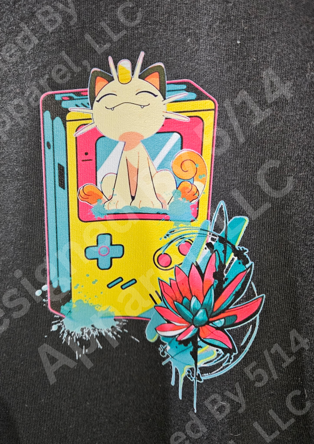 Close-up of Meowth retro Game Boy graphic — Meowth sitting on yellow Game Boy with pink lotus flower and teal paint splatter design by 5/14 Apparel