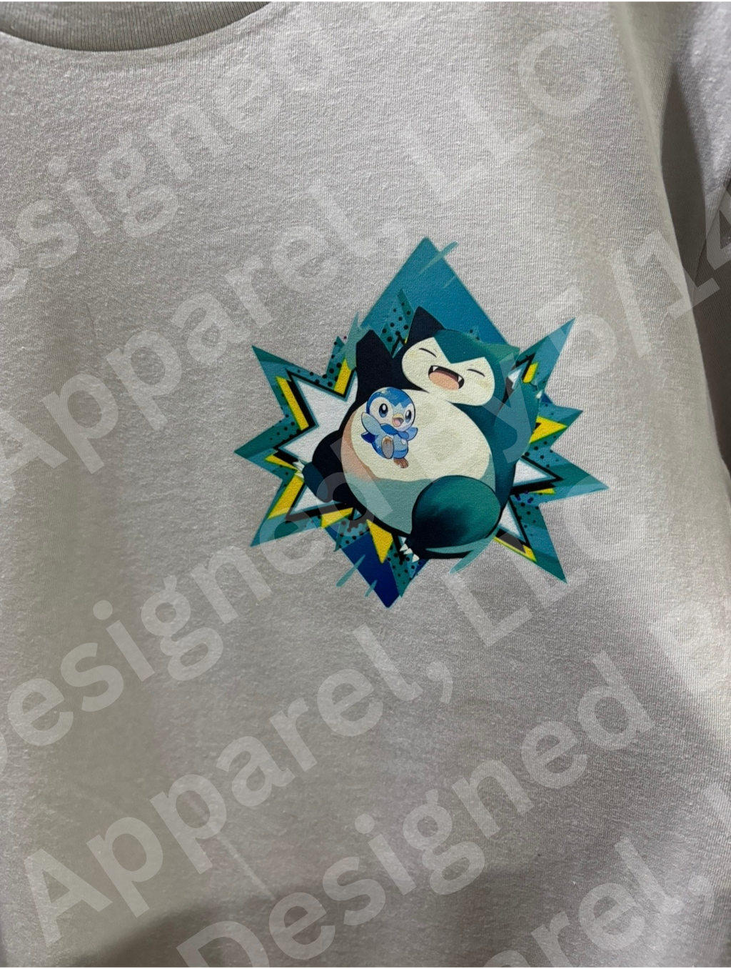Close-up of Snorlax and Piplup graphic on gray tee — Snorlax and Piplup in teal geometric starburst frame design by 5/14 Apparel